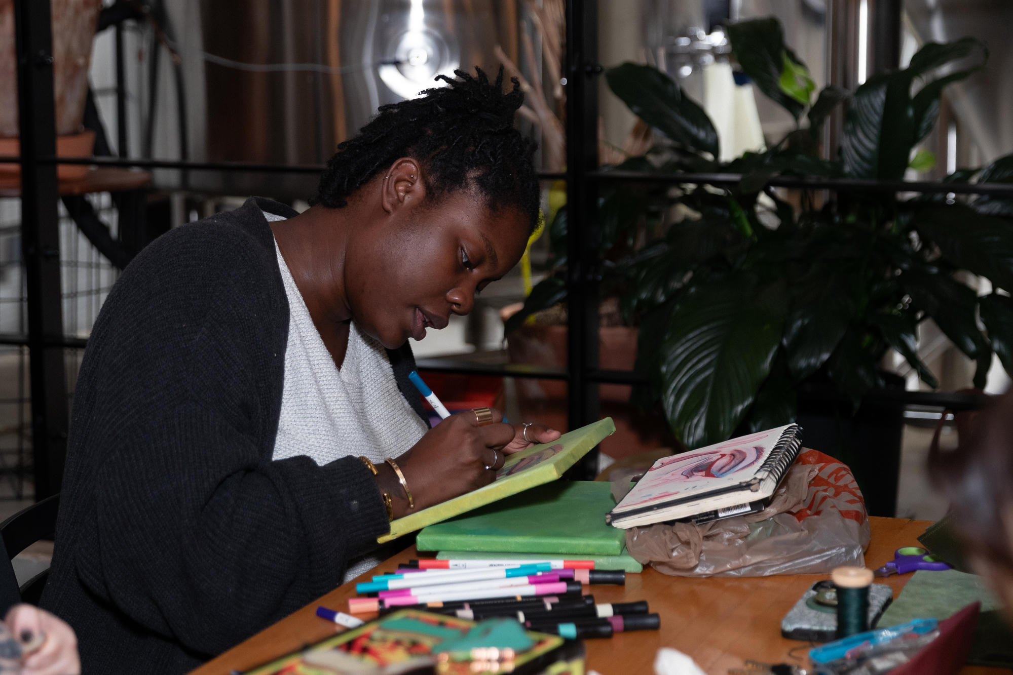 Artist drawing on a green canvas beside a sketchbook and colorful markers