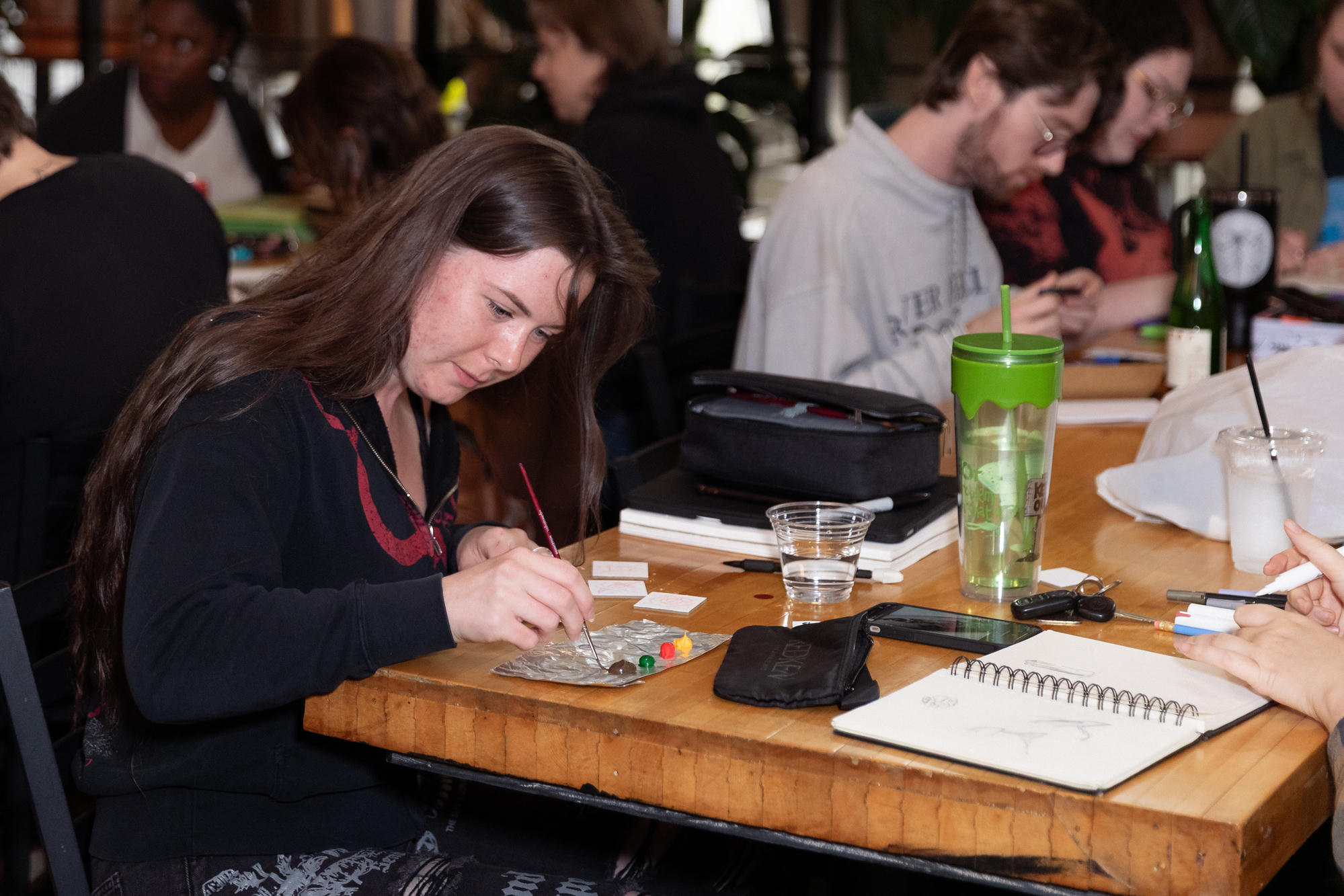 Artist mixing paint beside miniature canvases at a shared table